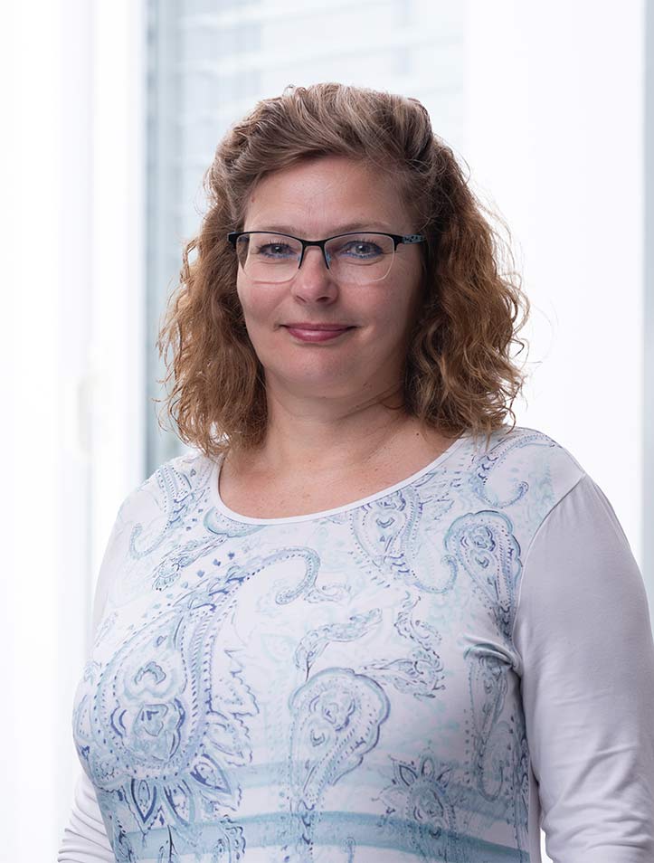 Frau mit Brille lächelt vor hellem Hintergrund.